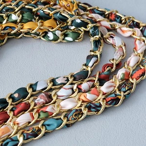 Detail of luxury gold metal chain intertwined with colorful silk scarf for handbags