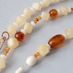 Detail of cream marbled acrylic and amber resin beads with a gold lobster clasp strap