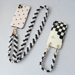 Dettaglio di cover per telefono a scacchi e pois con lunghe catene di perle bianche e nere