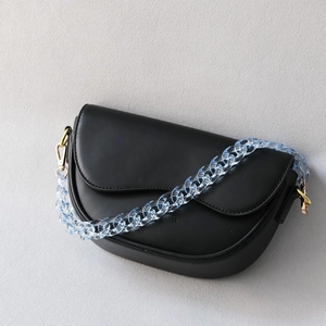 Detail of detachable blue acrylic resin chain on a black minimalist half-moon shoulder bag