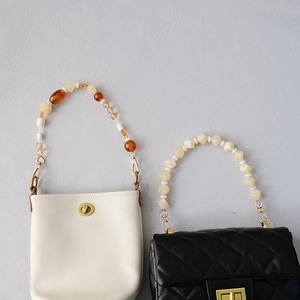 Detail view of acrylic bead handles on a white bucket bag and a black quilted purse