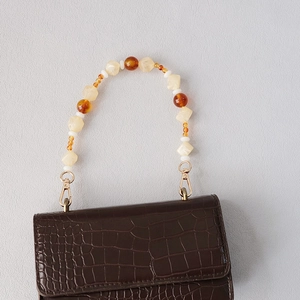 Detail of dark brown crocodile pattern handbag with decorative acrylic beaded handle