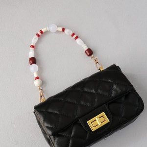 Detail of beaded handle on black quilted shoulder bag with golden twist lock closure