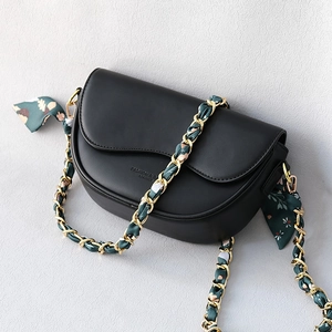 Detail of black saddle bag with golden chain strap entwined with a floral silk scarf