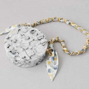 Détail du sac de soirée rond en acrylique marbré avec chaîne dorée et foulard