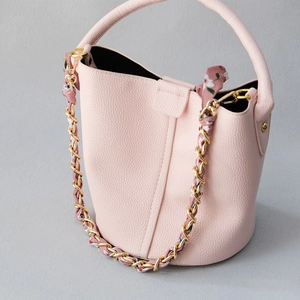 Détail du sac seau rose avec chaîne dorée et bandoulière tissée en foulard floral