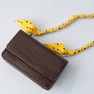 Détail du sac à main en cuir crocodile avec foulard en soie entrelacé dans la chaîne dorée
