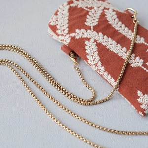 Detail of orange embroidered fabric pouch with elegant golden box chain strap and hook