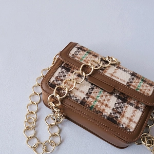 Close-up of vintage tweed fabric texture and heavy gold metal chain on small flap bag