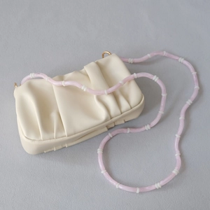Close-up of cream pleated handbag with pink acrylic beaded chain strap and gold hardware