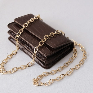 Macro shot of dark brown crocodile-embossed leather texture and gold chain strap detail