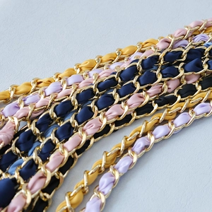 Detailed close-up of golden metal chains interwoven with colorful silk ribbons for handbags