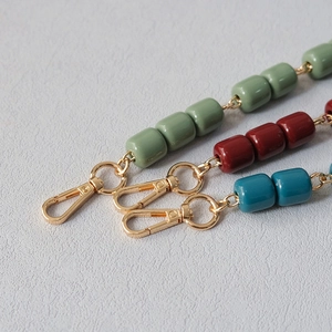 Detail view of handmade beaded acrylic bag straps in green, red, and blue with gold clasps