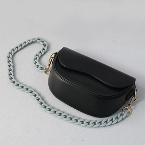 Detail view of a matte black saddle bag with chunky light blue acrylic chain strap