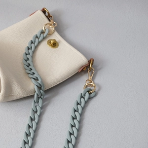 Close-up of off-white lychee leather bag with matte grey acrylic chain and gold metal clasp