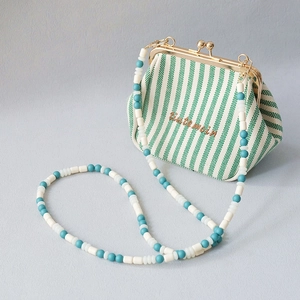 Detail of green striped canvas purse with retro metal clasp and long beaded shoulder strap