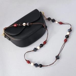 Detail of multi-colored acrylic bead shoulder strap on a sleek black crossbody handbag