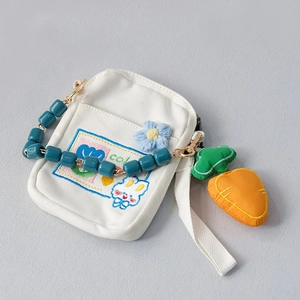 Detail of white canvas bag with blue bead handle, floral embroidery, and carrot charm