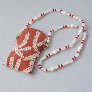 Detail of orange fabric phone pouch with white leaf embroidery and beaded chain strap