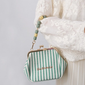 Detail of vintage canvas bag with green stripes and chunky beaded handle on white lace dress