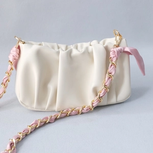 Close-up of cream pleated cloud bag with pink silk ribbon woven into gold chain strap