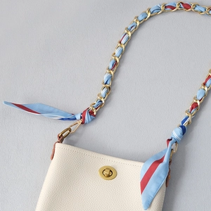 Dettaglio borsa in pelle crema con catena dorata intrecciata con foulard di seta a righe