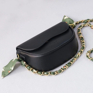 Dettaglio borsa a sella nera con catena dorata e tracolla in foulard di seta verde