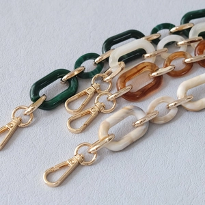 Detail of acrylic resin chain straps in marble grey, amber, and cream with gold metal clasps