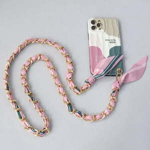 Dettaglio di un foulard in seta intrecciato con catena dorata e cover per cellulare