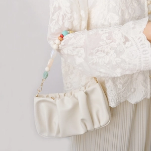 Detail of creamy white pleated cloud bag with colorful resin beaded handle and metal hook