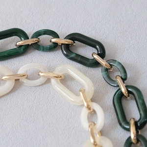 Detail of chunky acrylic link chain in dark green and white marble with gold rings