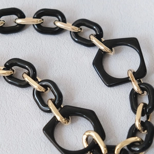 Detail shot of black resin geometric links paired with golden metal chain segments