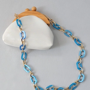 Detail of white faux leather mini pouch with wooden clasp and blue acrylic chain strap