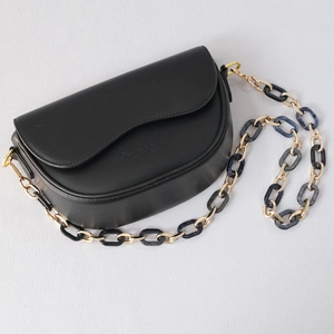 Detail of black matte saddle bag with unique gold metal and blue resin chain strap
