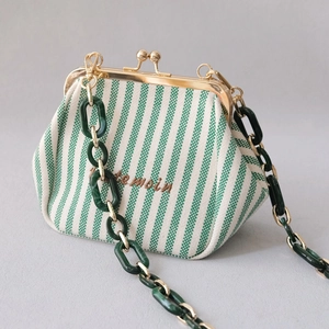 Detail of green striped canvas bag featuring acrylic chain and gold metal clasp