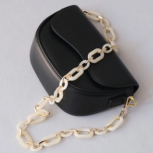 Detail of a black matte leather saddle bag with mixed gold and resin chain strap