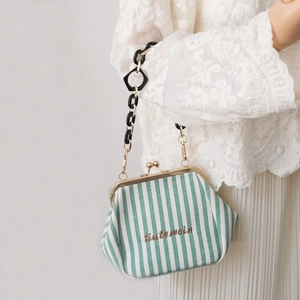 Close-up of green striped canvas kiss-lock bag with black acrylic chain on a model
