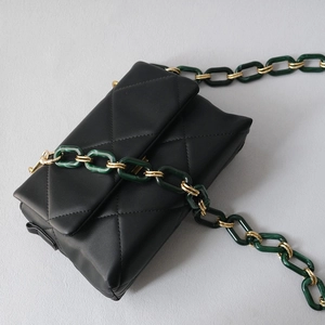 Detail of green marble acrylic and gold metal chain strap on black quilted bag