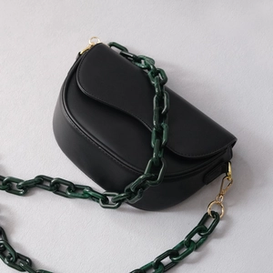 Detail of black matte saddle bag featuring a green marble acrylic chain and gold hardware