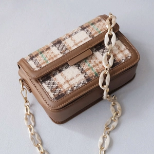 Detail of tweed flap bag featuring brown leather trim and marble acrylic chunky chain