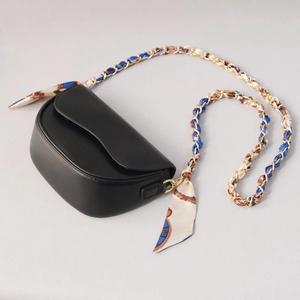 Detail of black saddle bag with golden chain strap entwined with blue silk scarf