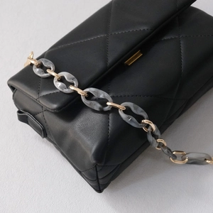 Detail of black quilted shoulder bag with resin marble and gold metal chain strap
