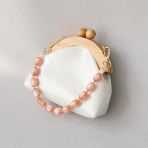 Detail of white scale-textured bag with wooden frame and pink bead handle strap