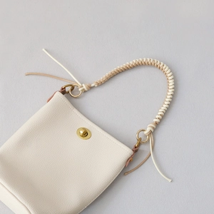 Close-up of cream leather bucket bag with brass twist lock and woven wax rope handle