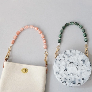 Detailed view of bead handles on ivory leather square bag and marble acrylic round bag
