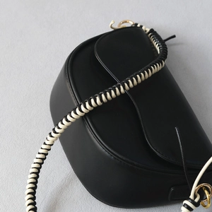 Minimalist black saddle bag with black and white woven strap and gold metal hardware