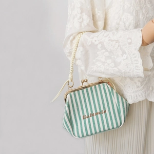 Close-up of green and white striped canvas bag with woven handle and gold hardware detail