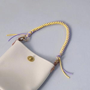 Detail view of woven wax rope handle and golden metal twist lock on white leather bag