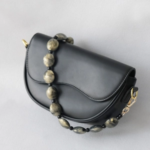 Close-up of black saddle bag featuring marble acrylic bead strap and gold hardware