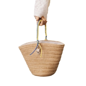 Handmade straw bucket bag featuring blue and yellow woven handles on a white background